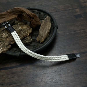 Detailed view of white braided leather bracelet with black magnetic clasp on wood