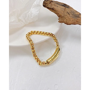 Nahaufnahme eines goldenen Box-Chain-Armbands mit Zylinderschließe auf weißer Keramik