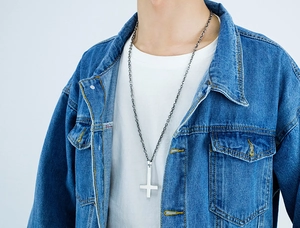 Close-up of a silver inverted cross pendant on a thick round link chain worn by a model