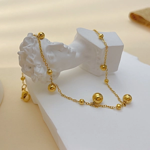 Goldenes Fußkettchen mit polierten Edelstahlkugeln auf einer weißen klassischen Statue