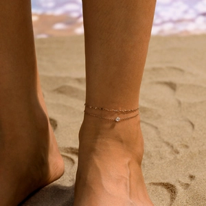 Vue détaillée d'une chaîne de cheville double couche dorée avec zircon sur la plage