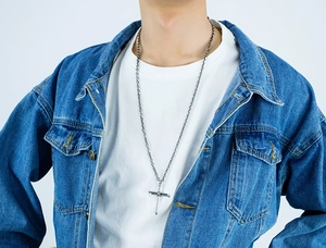 Close-up of a men's punk style stainless steel cross and sword pendant on a model