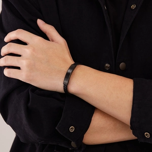 Primer plano de una pulsera de cuero trenzado negro con placa de metal mate en la muñeca