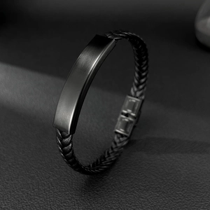 Detalle de una pulsera de cuero trenzado negro con placa de metal cepillado y cierre