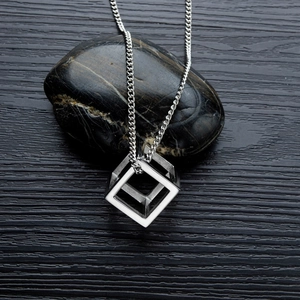 Detailed view of a geometric hollow cube pendant on a sleek chain over dark stones