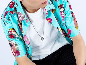 Detailed view of hollow cube pendant necklace on a model wearing a green printed shirt