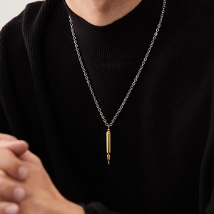 Gros plan d'un pendentif balle dorée sur chaîne argentée porté sur un pull noir pour homme