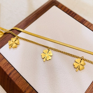 Detail eines doppellagigen goldenen Kleeblatt-Fußkettchens mit Schlangenkette und Gravuren