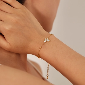 Dettaglio di un bracciale a farfalla dorato con madreperla bianca e zircone sul polso