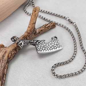 Détail du pendentif couperet en acier avec crâne sur une branche de bois rustique