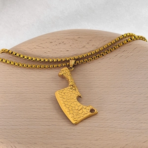 Détail du pendentif couperet en acier doré avec texture rustique sur chaîne box