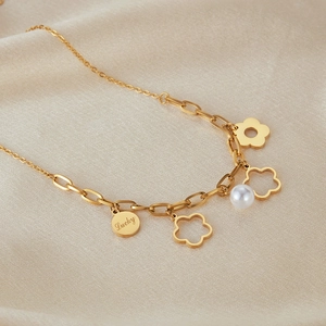 Dettaglio macro della collana d'oro con ciondolo Lucky, fiori e perla bianca