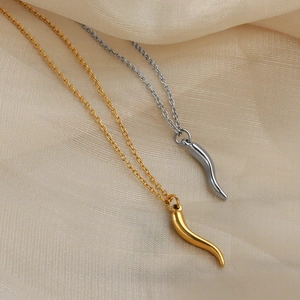 Polished gold and silver cornicello chili pendant necklaces on beige silk background