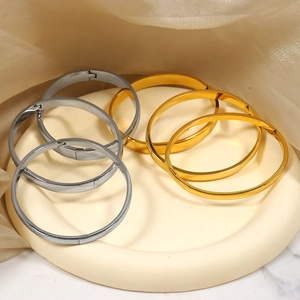 Minimalist gold and silver stainless steel hinged bangles on elegant beige jewelry tray