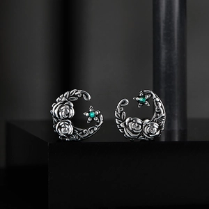 Macro detail of vintage silver moon earrings featuring rose engraving and green star stone