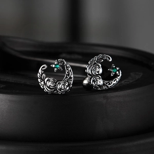 Macro shot of silver crescent moon earrings with vintage rose and green gemstone