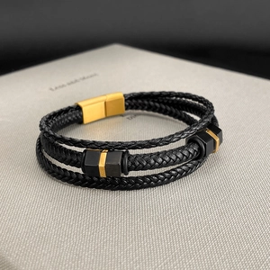 Close-up of triple-layer black braided leather bracelet with golden magnetic clasp