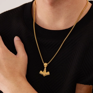 Gros plan détaillé du pendentif Mjölnir doré avec motifs vikings sur pull noir