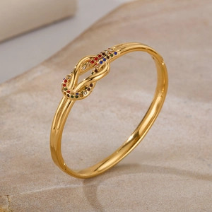 Dettaglio di un bracciale dorato con nodo e zirconi colorati su una base di marmo