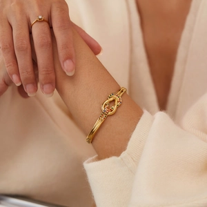 Dettaglio ravvicinato di un bracciale a nodo dorato con strass colorati su uno sfondo caldo