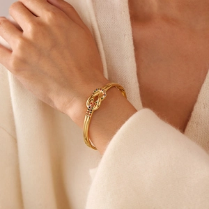 Dettaglio del bracciale a nodo dorato con zirconi colorati indossato su un maglione
