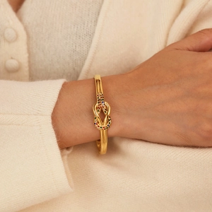Elegante bracciale a nodo dorato con zirconi multicolore su sfondo in maglia beige