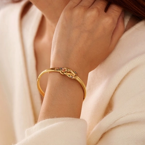 Dettaglio di un bracciale a nodo dorato con cristalli colorati sul polso di una donna