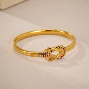 Bracciale a rigido con nodo dorato e strass colorati su sfondo di tessuto strutturato