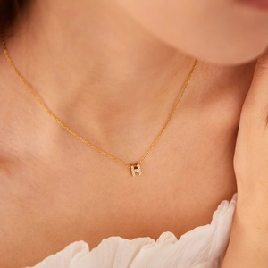 Close-up of gold-plated letter H necklace pendant with sparkling pavé zircons on a model