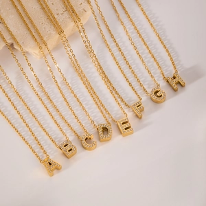 Golden stainless steel letter necklaces with zircon stones A to H displayed on stone