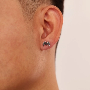 Macro shot of gothic steel bat wings earring with black heart zircon on male ear lobe
