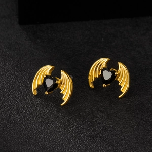Gothic gold wings earrings with black heart zircon stones on dark textured surface