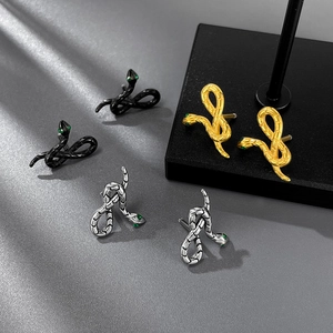Detailed view of snake-shaped earrings in black, gold, and silver with green gem eyes
