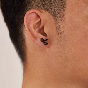 Close-up of a matte black snake stud earring with green stone eyes worn on the ear