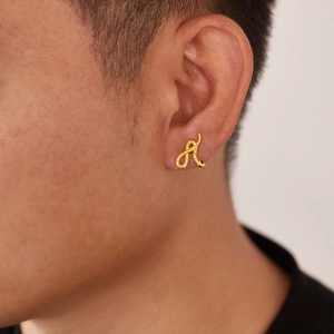 Close-up of golden snake stud earring with green gemstone eyes on male model ear