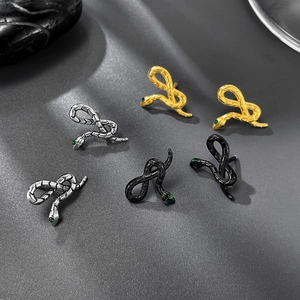 Three snake earrings in gold, silver, and black with green gemstone eyes on dark background