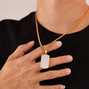 Gros plan d'une chaîne box dorée et d'un pendentif rectangulaire bicolore sur t-shirt