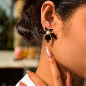 Détail de boucle d'oreille fleur en émail noir et perle portée par un modèle féminin