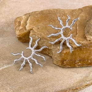 Makroaufnahme von silbernen Edelstahl-Ohrringen im Sonnendesign auf Naturstein