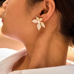Détail d'une élégante boucle d'oreille fleur en émail blanc avec perle portée par un mannequin