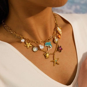 Dettaglio di collana dorata a strati con ciondoli a stella marina, tartaruga e delfino