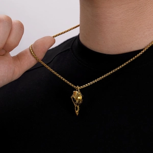 Close-up of a gold-plated bird skull pendant with box chain on a male model
