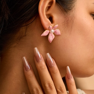 Boucles d'oreilles fleurs dorées avec pétales marbrés roses et perle sur un mannequin