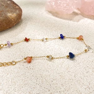 Dettaglio del bracciale a catena dorata con pietre naturali su superficie sabbiosa