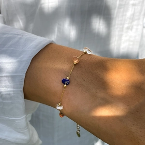 Dettaglio di un bracciale a catena dorata con pietre grezze colorate sul polso