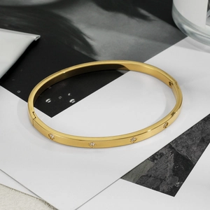 Detail of a polished gold-plated stainless steel oval bangle set with four round cubic zirconia
