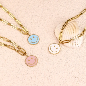 Three smiley face pendant necklaces with gold paperclip chains in blue pink and white