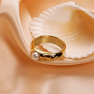 Close-up of hammered gold stainless steel ring with a white pearl on silk fabric