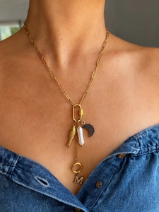 Detail van gouden schakelketting met vis, parel en kristallen letter M hanger bedeltjes