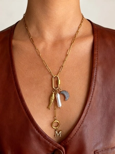 Detail van gouden paperclip ketting met parel, vis en M-hanger gedragen door een model